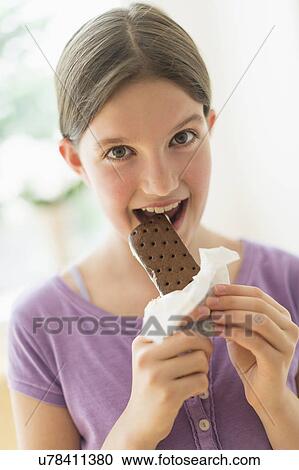 Stock Image - girl (10-11) eating ice cream sandwich. Fotosearch
