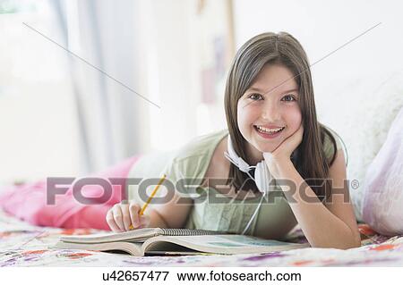 Stock Photo - girl (10-11) lying in bed and learning. Fotosearch