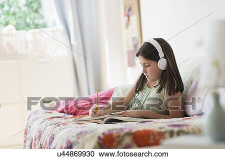 Stock Image - girl (10-11) lying in bed and writing in notebook. Fotosearch