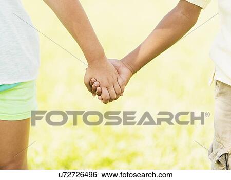 Stock Photograph - girl ( 8-9) and boy (6-7) holding hands, close up. Fotosearch