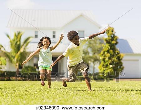 Stock Image - girl (8-9) and boy (6-7) playing on front yard. Fotosearch