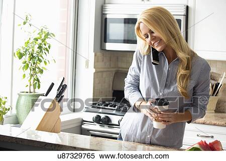 Stock Photography - Happy woman talking on mobile phone in kitchen. Fotosearch