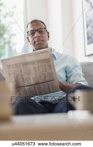 Stock Image - Man reading newspaper on sofa. Fotosearch
