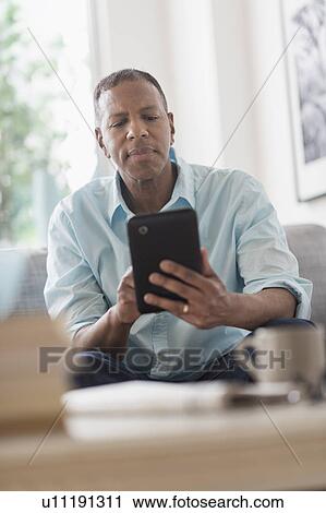 Man sitting on sofa at home and using digital tablet View Large Photo Image Stock Image - Man sitting on sofa at home and using digital tablet. Fotosearch