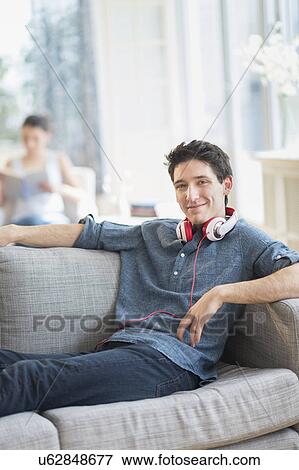 Man sitting on sofa, woman in background View Large Photo Image Stock Photo - Man sitting on sofa, woman in background. Fotosearch