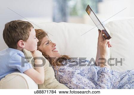 Mother and son (6-7) lying on sofa using digital tablet View Large Photo Image Picture - Mother and son (6-7) lying on sofa using digital tablet. Fotosearch