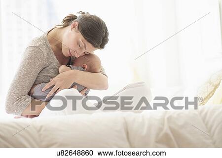 Stock Image - Mother embracing baby boy (2-5 months) in bed. Fotosearch