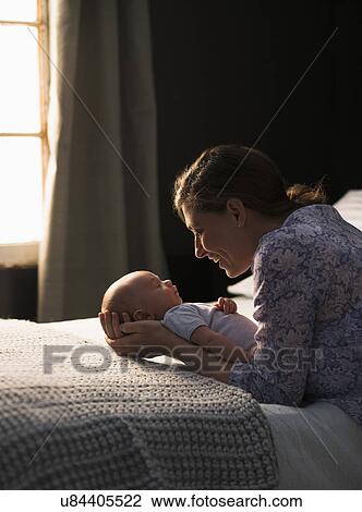 Stock Image - Mother holding baby boy (2-5 months) in bedroom. Fotosearch