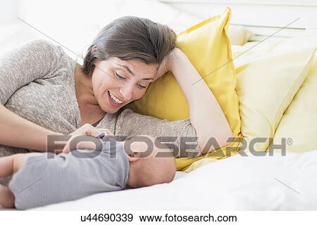 Stock Photo - Mother with baby boy (2-5 months) lying on bed. Fotosearch