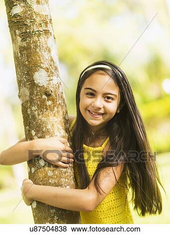 Stock Photo - Portrait of girl ( 8-9) hugging tree trunk. Fotosearch