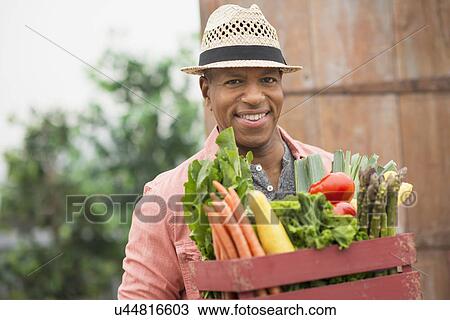 Stock Image - Portrait of man carrying crate full of fresh vegetables. Fotosearch