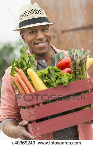Stock Photo - Portrait of man carrying crate full of fresh vegetables. Fotosearch