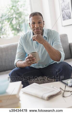 Stock Photo - Portrait of man sitting on sofa at home. Fotosearch