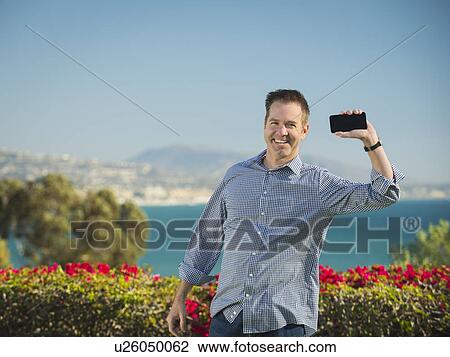 Portrait of smiling man holding smartphone View Large Photo Image Stock Image - Portrait of smiling man holding smartphone. Fotosearch