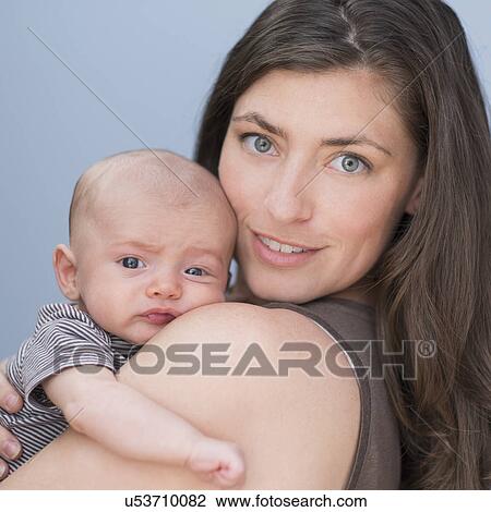 Stock Image - Portrait of smiling mother holding baby boy (2-5 months) on her arm. Fotosearch