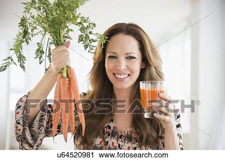 Stock Image - Portrait of woman holding carrots and carrot juice. Fotosearch