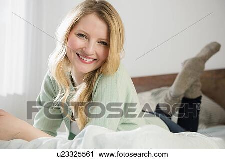 Stock Image - Portrait of woman lying on bed. Fotosearch