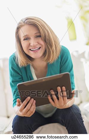 Stock Photograph - Portrait of woman on sofa holding digital tablet. Fotosearch