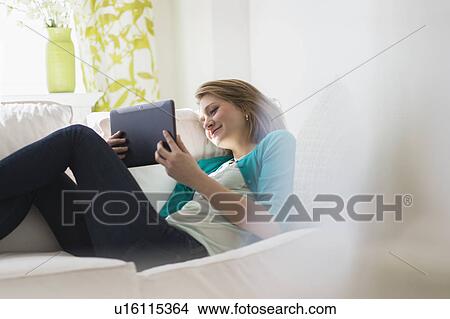 Picture - Portrait of woman on sofa using digital tablet. Fotosearch