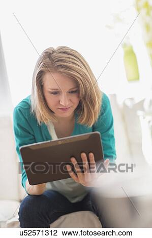 Stock Image - Portrait of woman on sofa using digital tablet. Fotosearch