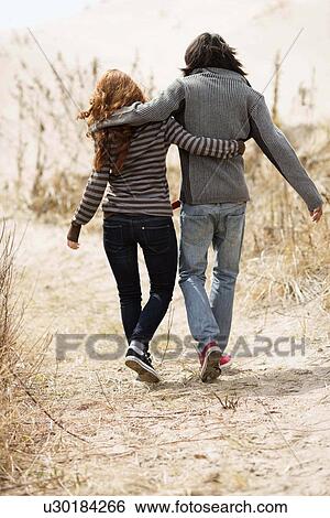 Rear view of couple walking on dirt road View Large Photo Image Stock Photograph - Rear view of couple walking on dirt road. Fotosearch