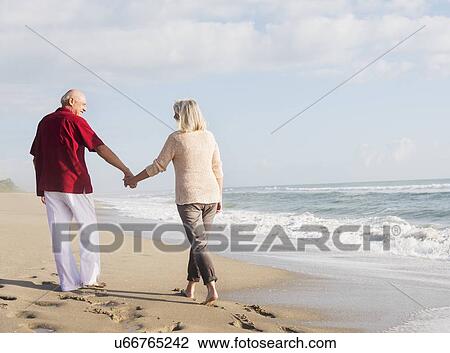 Stock Image - Senior couple walking on beach. Fotosearch