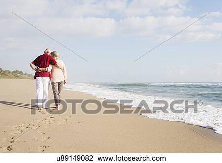Stock Image - Senior couple walking on beach. Fotosearch