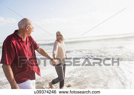 Stock Photograph - Senior couple walking on beach. Fotosearch