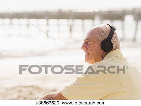 Senior man with headphones sitting on beach View Large Photo Image Stock Image - Senior man with headphones sitting on beach. Fotosearch