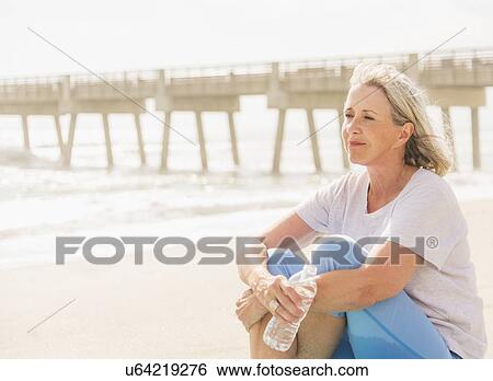 Stock Photograph - Senior woman sitting on beach. Fotosearch