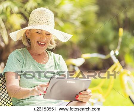 Stock Image - Senior woman using digital tablet in park. Fotosearch