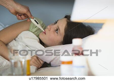 Stock Image - Sick girl (8-9) with thermometer in mouth. Fotosearch