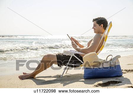Side view of man sitting on deckchair and using digital tablet View Large Photo Image Stock Photo - Side view of man sitting on deckchair and using digital tablet. Fotosearch