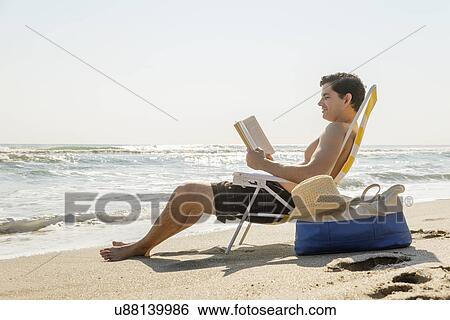 Side view of man sitting on deckchair and reading book View Large Photo Image Stock Photograph - Side view of man sitting on deckchair and reading book. Fotosearch