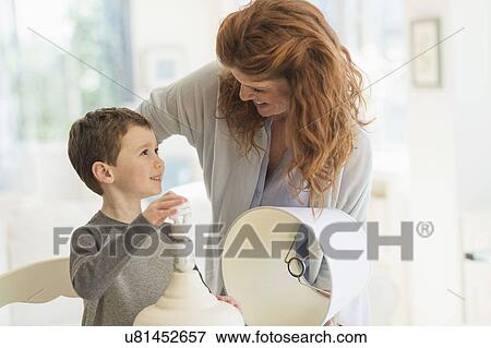 Stock Photo - son (6-7) and mother changing lightbulb in table lamp. Fotosearch