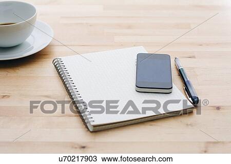 Stock Image - Spiral notebook, Ballpoint pen, Mobile phone and coffee cup on wooden table. Fotosearch