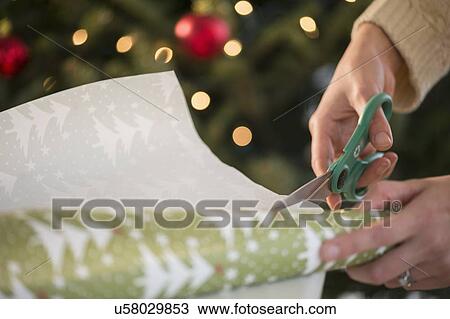 Stock Image - Studio Shot of female's hands cutting wrapping paper. Fotosearch