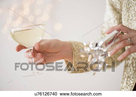 Stock Image - Studio Shot of female's hands holding champagne and noisemaker. Fotosearch