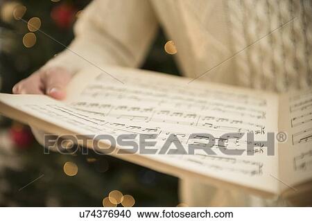 Stock Image - Studio Shot of woman holding sheet music at christmas. Fotosearch