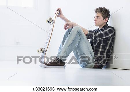 Stock Image - Teenage boy (16-17) holding skateboard. Fotosearch