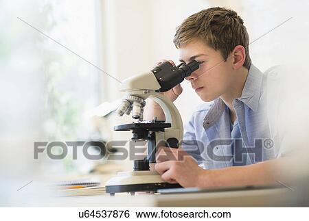Stock Photograph - Teenage boy (16-17) looking through microscope. Fotosearch