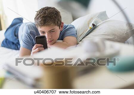 Stock Photo - Teenage boy (16-17) lying on bed and text messaging. Fotosearch