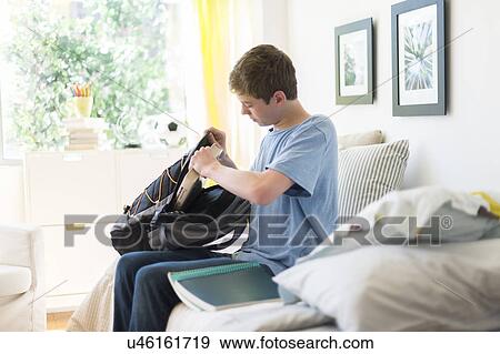 Stock Photo - Teenage boy (16-17) packing books into backpack. Fotosearch