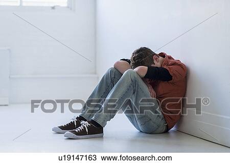 Stock Image - Teenage boy (16-17) sitting in hallway. Fotosearch