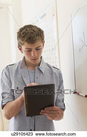 Stock Image - Teenage boy (16-17) using digital tablet in classroom. Fotosearch