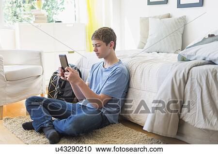 Stock Image - Teenage boy (16-17) using digital tablet in bedroom. Fotosearch
