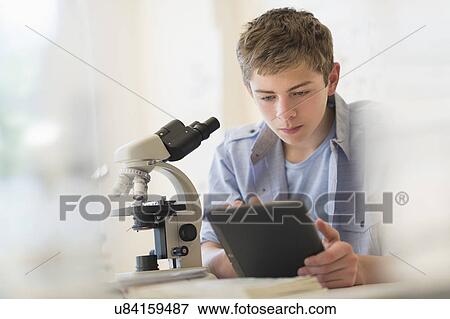 Stock Photo - Teenage boy (16-17) using digital tablet in laboratory. Fotosearch