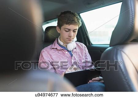 Stock Photo - Teenage boy (16-17) using digital tablet in car. Fotosearch