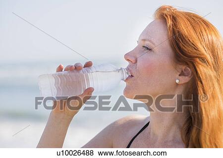 Stock Photo - View of woman drinking water on beach. Fotosearch