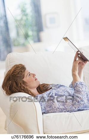 Stock Photograph - Woman lying on sofa and using laptop. Fotosearch